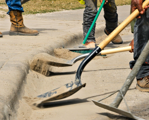 Several workers use shovels and broom to clean dirt off the street by the sidewalk at a work site